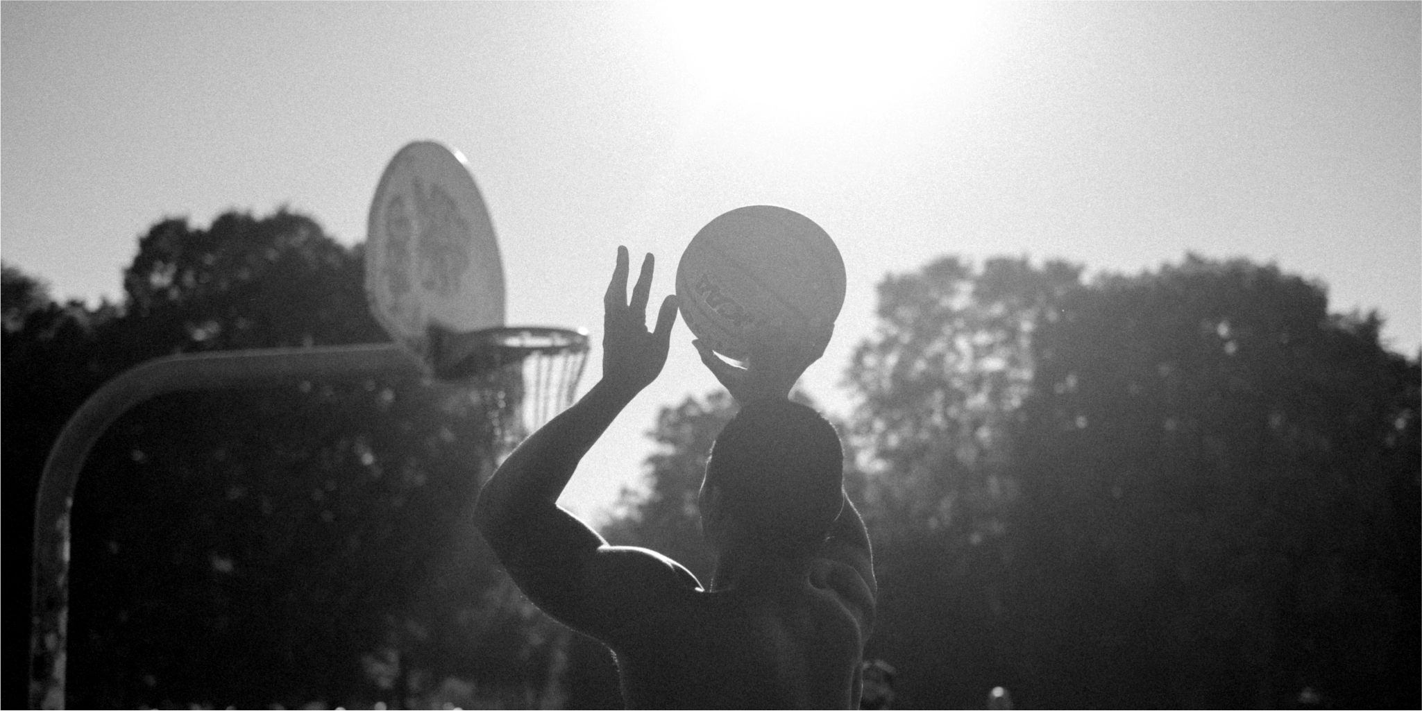 Ein Mann fängt einen Frisbee auf einem Basketballplatz, umgeben von Naturelementen.